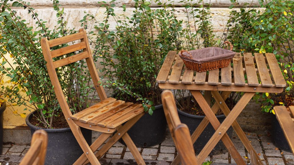 A wooden table and chair among green plants with raindrops